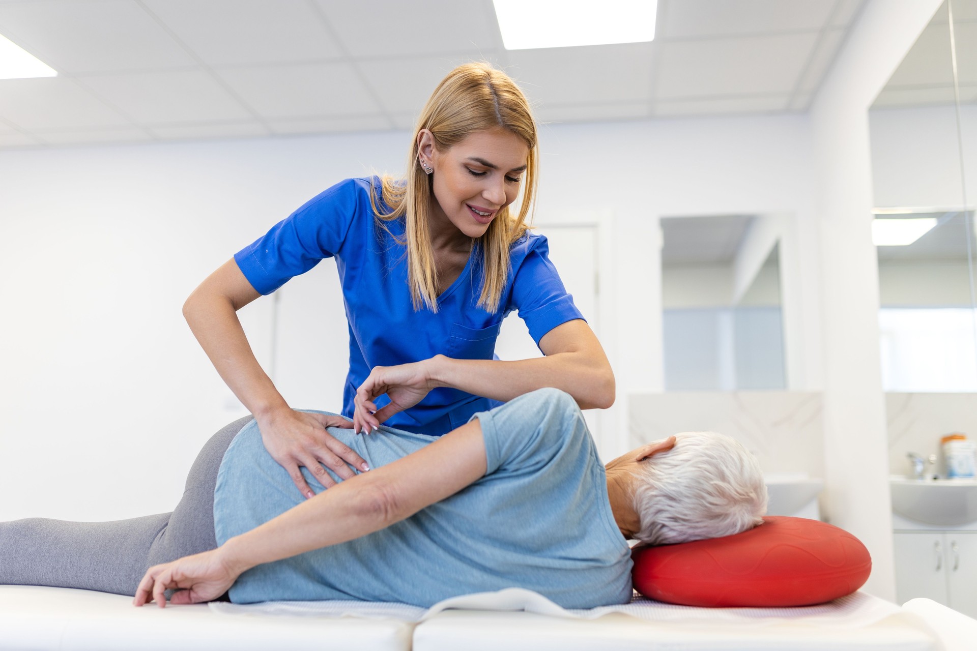 Young doctor chiropractor or osteopath fixing lying senior woman back with hands movements during visit in manual therapy clinic. Professional chiropractor during work